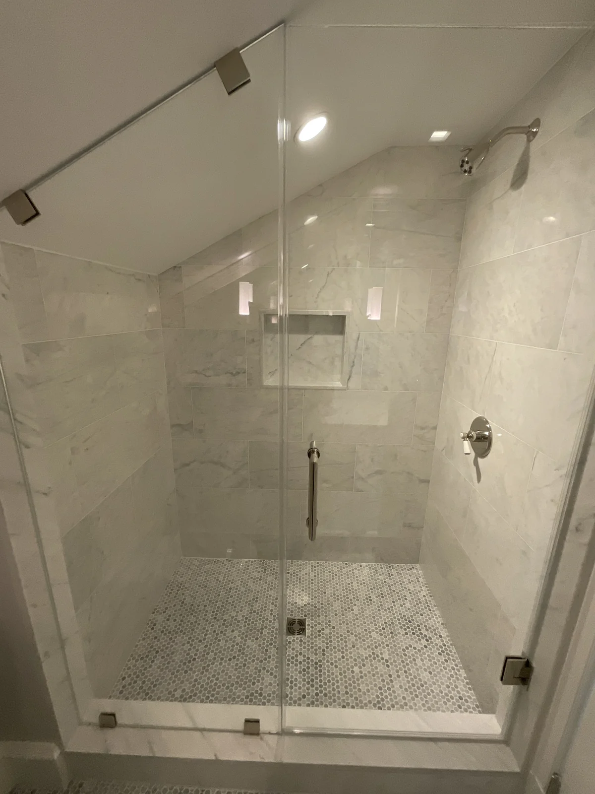 Completed tile shower with a recessed niche, glass enclosure and mosaic floor